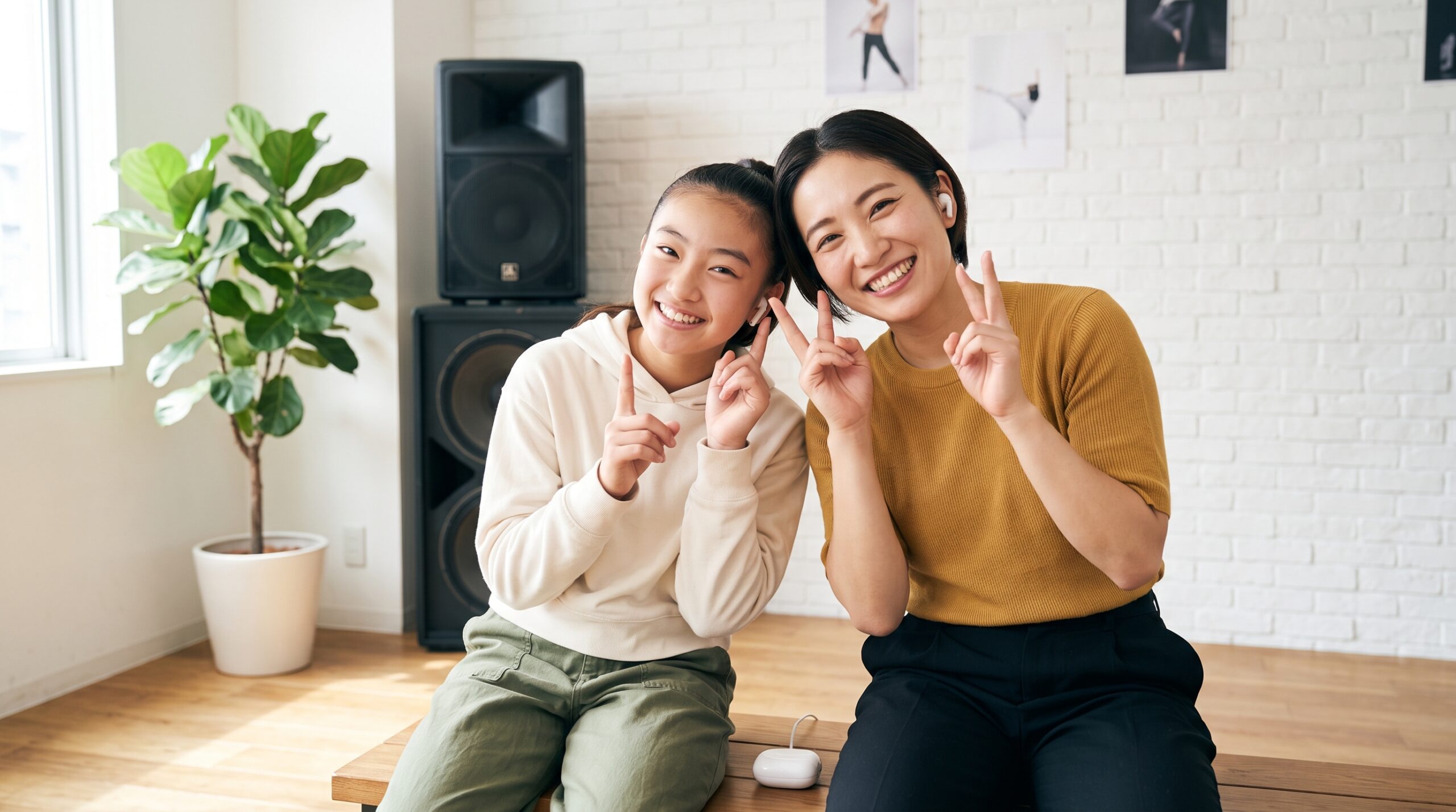 スピーカーの横で、片耳ずつイヤホンを分け合って音楽を聴く生徒と講師